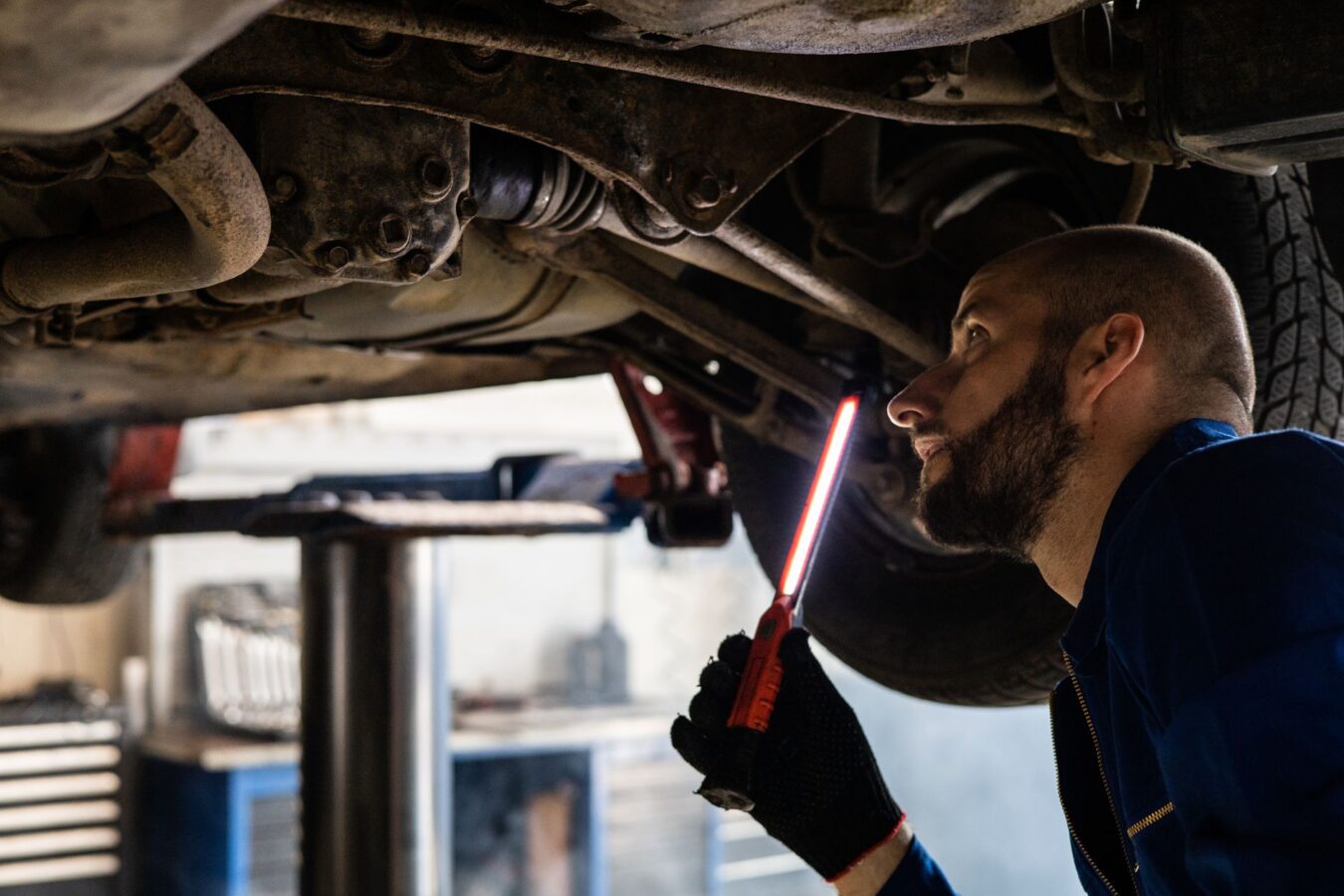 Mechanic inspecting transmission oil leak under car on lift